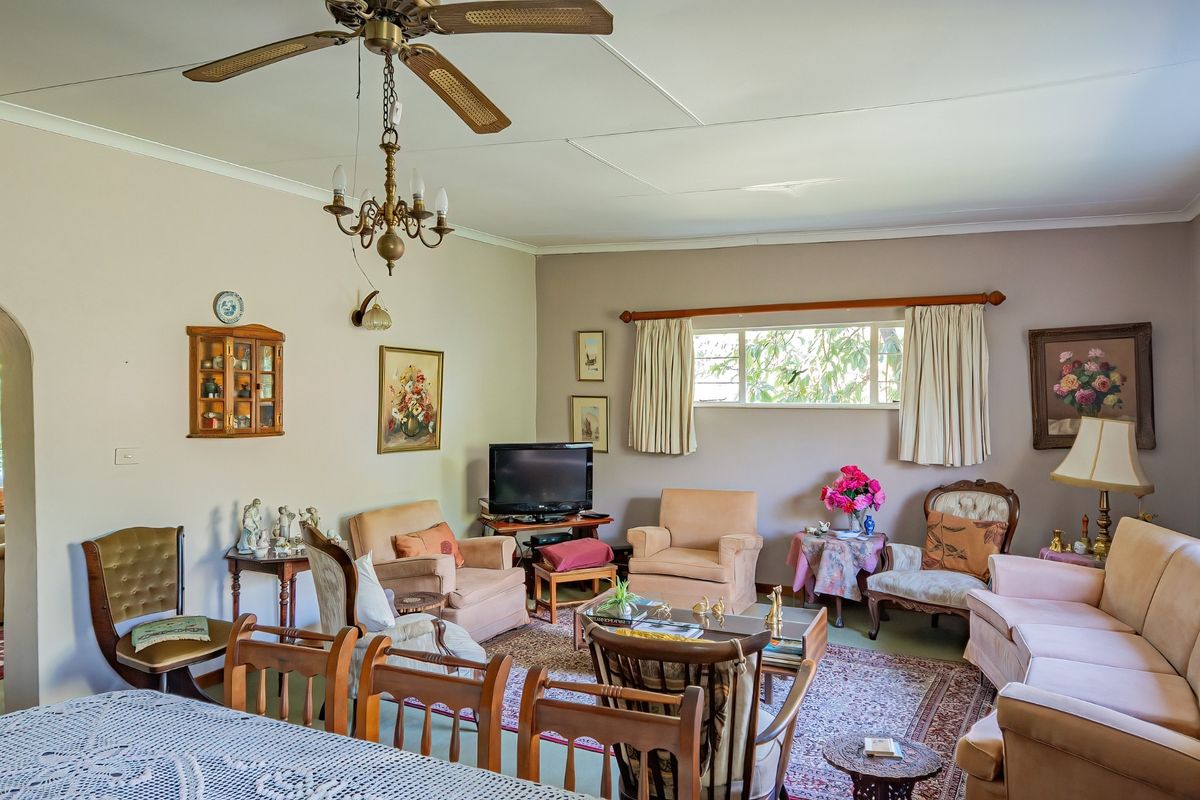 A spacious living room featuring a ceiling fan, chandelier, and large window, offering a comfortable and traditional living space.