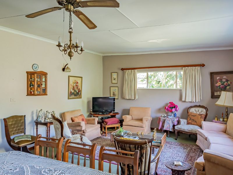 A spacious living room featuring a ceiling fan, chandelier, and large window, offering a comfortable and traditional living space.