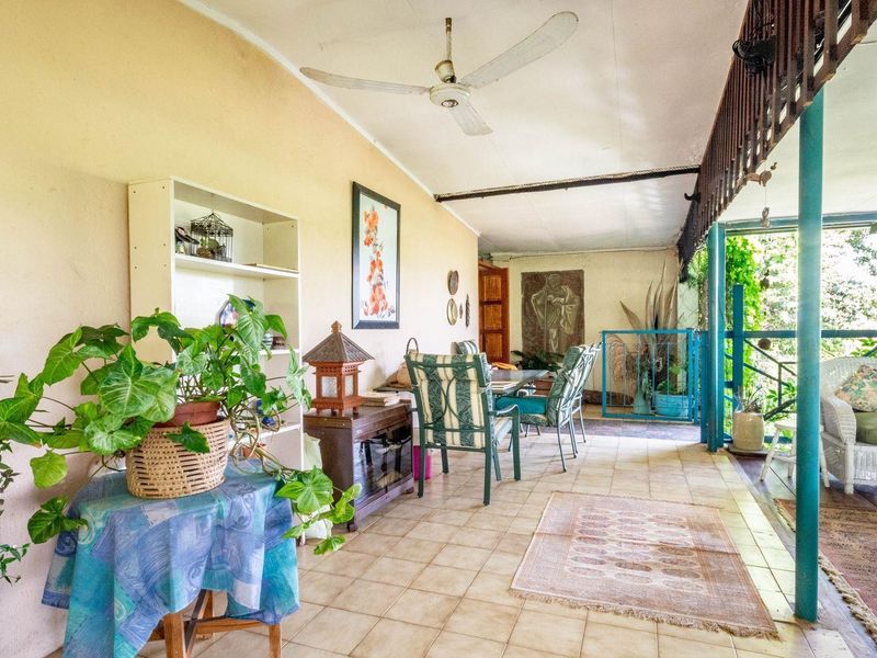 A covered outdoor patio area featuring tiled flooring, a ceiling fan, and structural support columns, offering a functional space for outdoor relaxation.