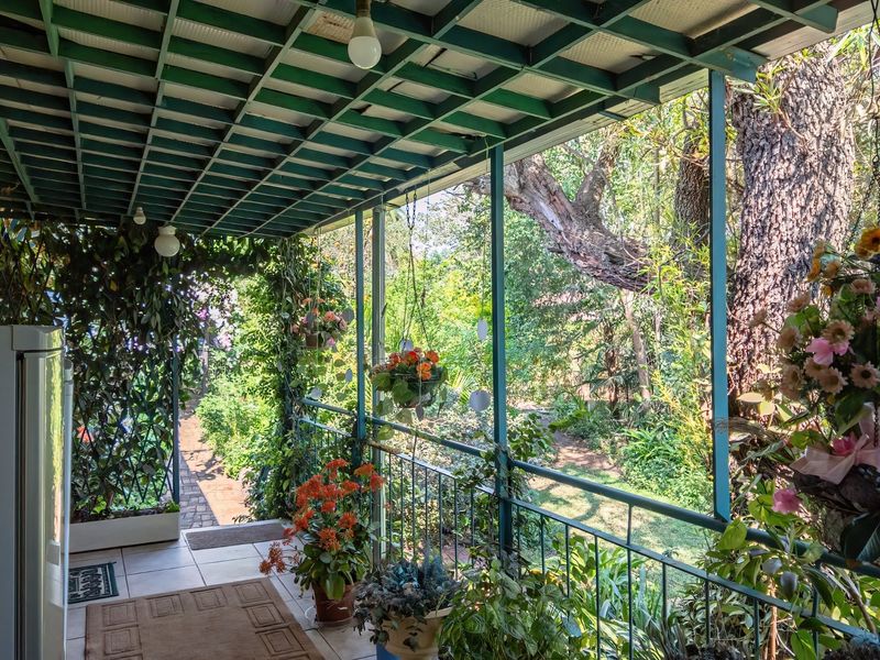 A covered outdoor patio area featuring tiled flooring, a metal pergola roof structure, and metal railings, overlooking a lush garden setting.