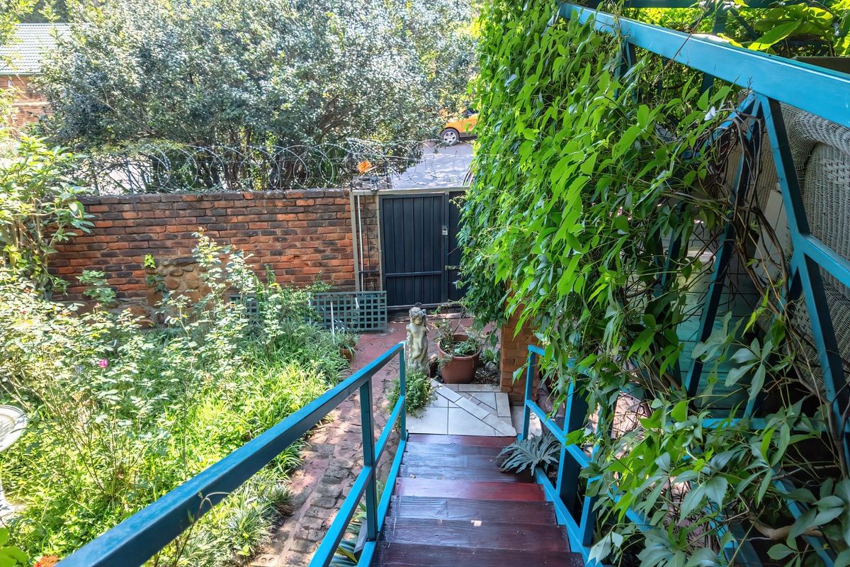 A view looking down a metal staircase into a rear garden area featuring a brick boundary wall with security razor wire and a pedestrian gate.