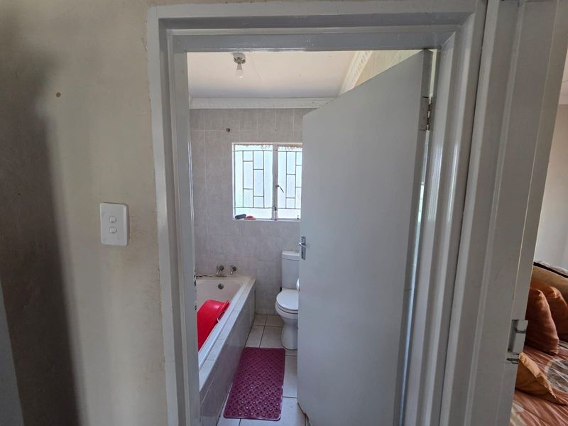A functional bathroom featuring a built-in bathtub, toilet, and tiled finishes, requiring cosmetic updates to improve its overall condition and aesthetic appeal.