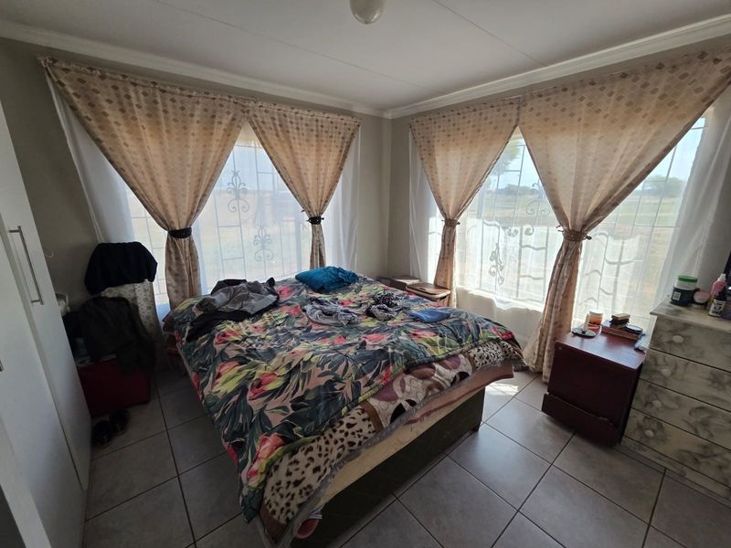 A functional bedroom featuring tiled flooring, built-in cupboard storage, and large windows fitted with security bars for added safety.