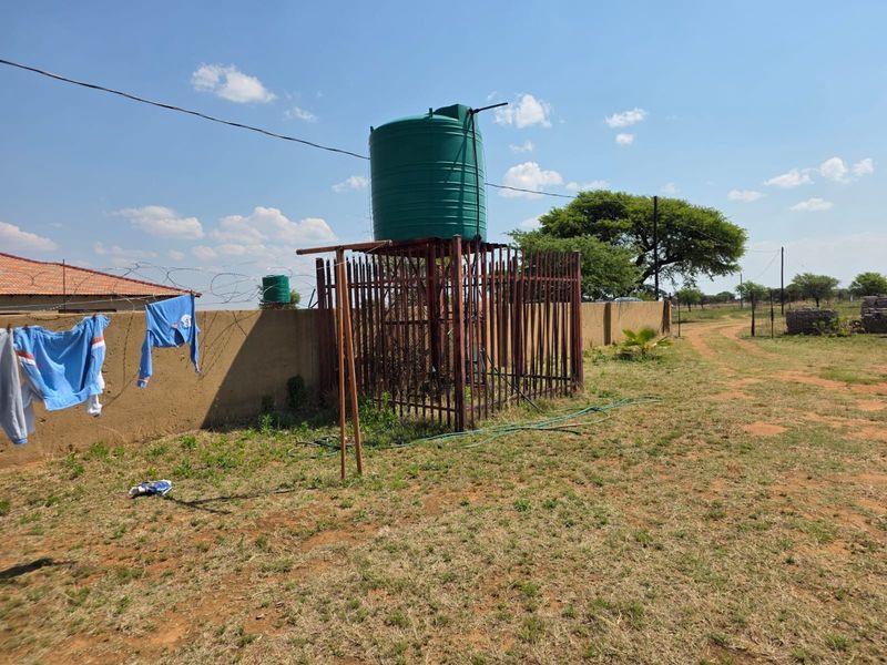 Outdoor area featuring a water storage tank on a metal stand, enclosed by a perimeter wall with security razor wire.