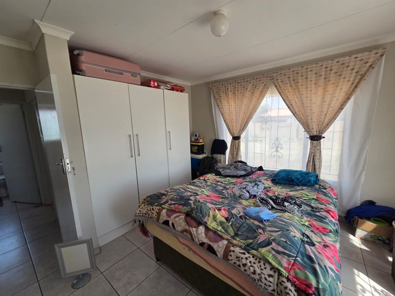 A functional bedroom featuring tiled flooring, a built-in wardrobe, and a window fitted with a security gate.