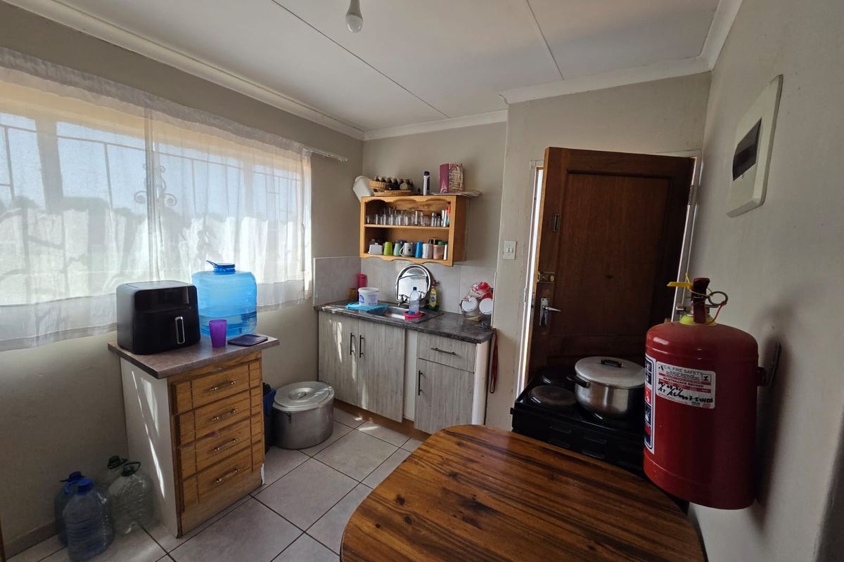 A functional kitchen area featuring tiled flooring, built-in cabinetry with laminate countertops, a stainless steel sink, and security bars on the window.