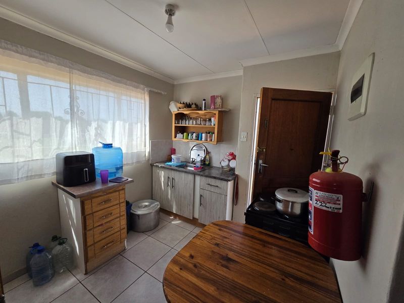 A functional kitchen area featuring tiled flooring, built-in cabinetry with laminate countertops, a stainless steel sink, and security bars on the window.