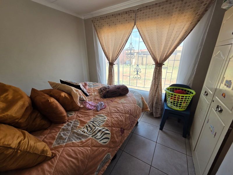 A functional bedroom featuring tiled flooring, a built-in wardrobe, and security burglar bars on the window.