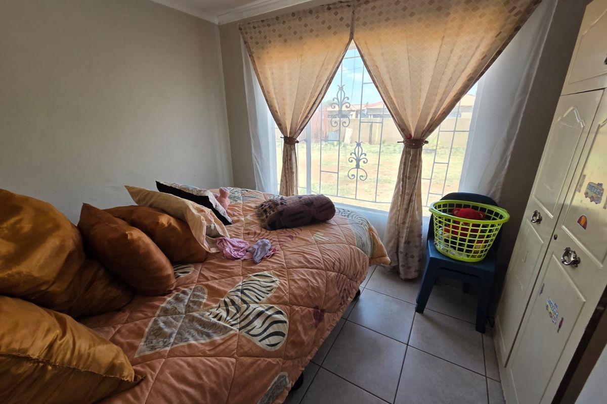 A functional bedroom featuring tiled flooring, a built-in wardrobe, and security burglar bars on the window.