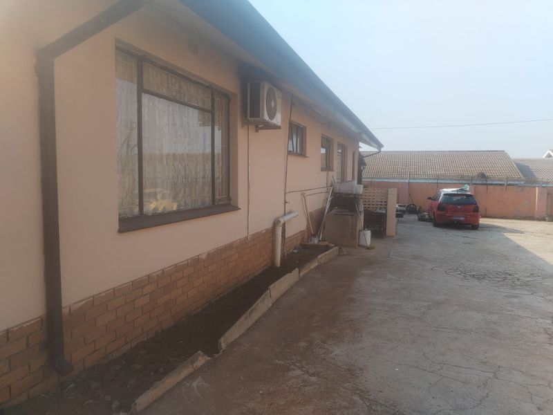Rear exterior view of the property featuring a concrete driveway, brick base detailing, and wall-mounted air conditioning unit.