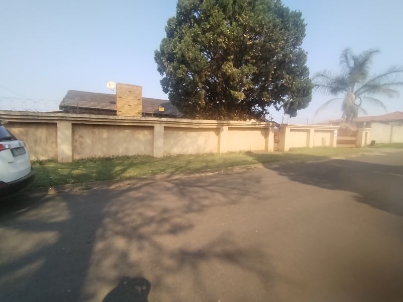 Street view of the property showing the perimeter wall, razor wire security, and a glimpse of the tiled roof and chimney.