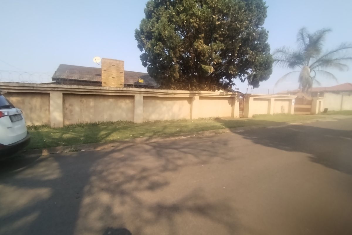 Street view of the property showing the perimeter wall, razor wire security, and a glimpse of the tiled roof and chimney.