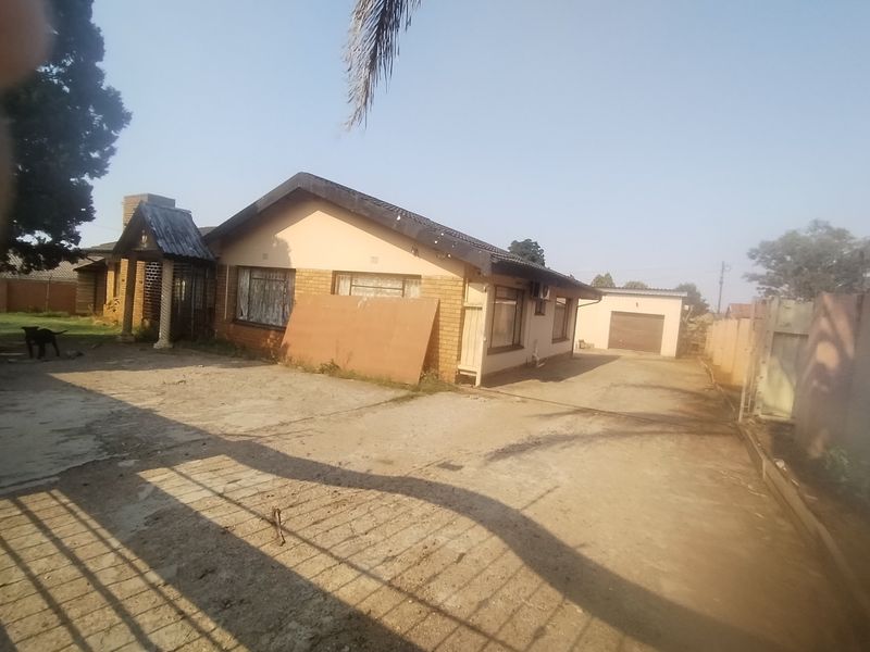 Front view of a single-story brick house featuring a concrete driveway, detached garage, and perimeter walling.