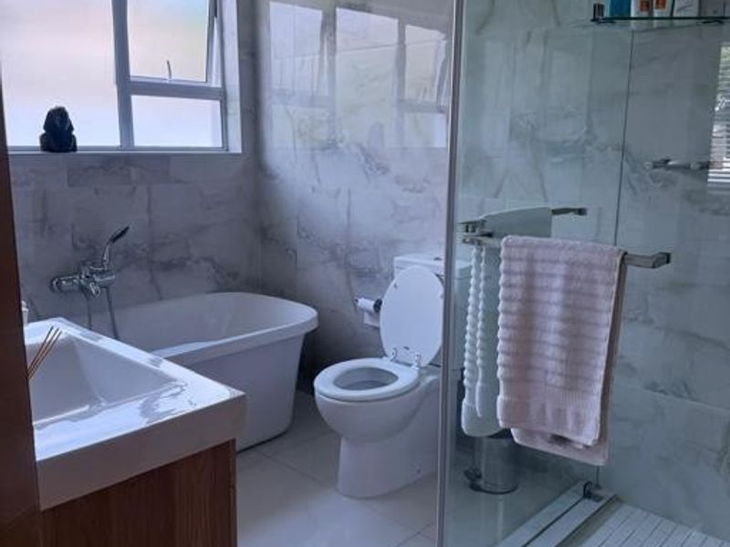 Modern bathroom featuring a freestanding bathtub, glass-enclosed shower, vanity cabinet with basin, and contemporary marble-look wall tiling.