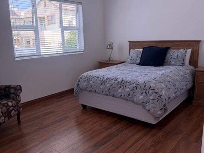 A well-maintained bedroom featuring warm-toned laminate flooring, recessed ceiling lighting, and venetian blinds, offering a clean and functional living space.