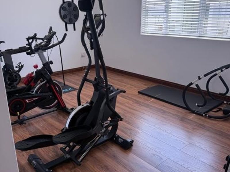 A dedicated home gym space featuring durable laminate flooring and large windows with fitted venetian blinds.