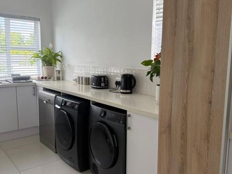A modern, well-maintained laundry area featuring sleek white cabinetry, stone countertops, tiled backsplash, and integrated appliance spaces with polished floor tiles.