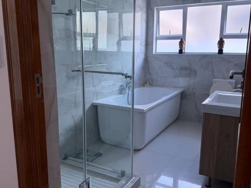 Modern bathroom featuring a glass-enclosed shower, a sleek freestanding bathtub, a vanity unit, and elegant marble-look wall tiling.