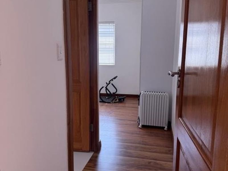 A clean, well-maintained hallway featuring warm-toned laminate flooring, classic wooden door frames, and decorative coving throughout the transition space.