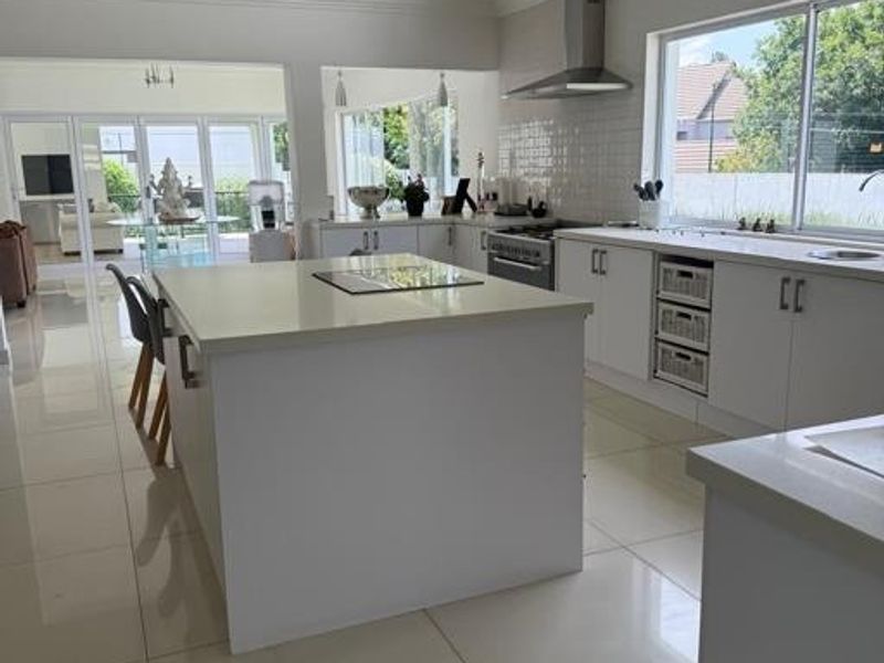 Modern kitchen featuring a central island, stone countertops, stainless steel appliances, and sleek white cabinetry with polished tile flooring.