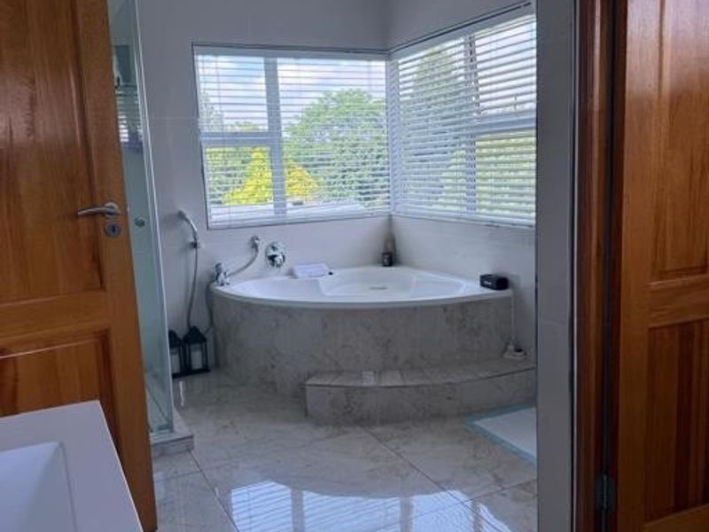 A bright bathroom featuring a corner bathtub, tiled flooring, a glass shower enclosure, and wooden doors, offering a clean and functional space.