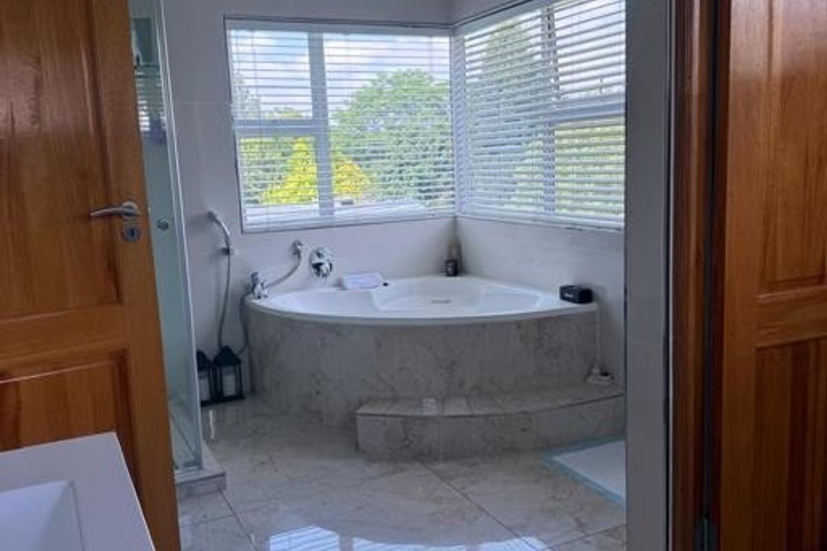 A bright bathroom featuring a corner bathtub, tiled flooring, a glass shower enclosure, and wooden doors, offering a clean and functional space.