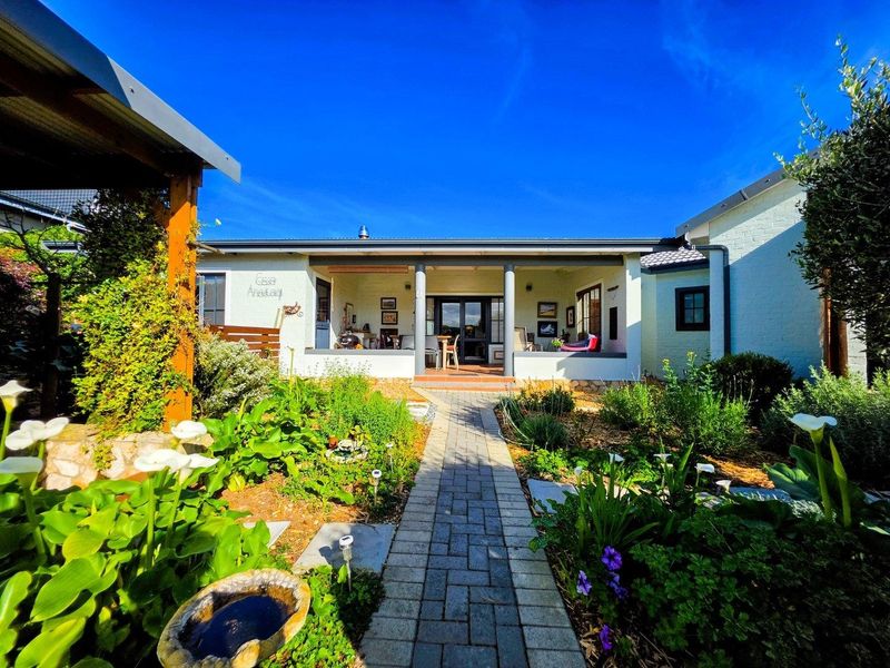 A well-maintained rear exterior view featuring a covered patio, a brick-paved pathway, and a lush, landscaped garden under a clear blue sky.