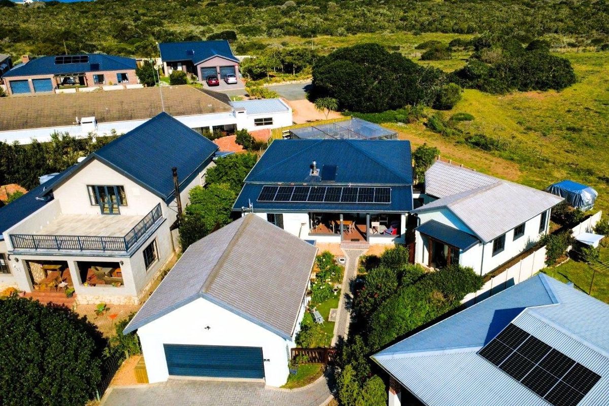 Aerial view of the property showcasing multiple buildings, solar panel installations, paved driveway, and surrounding coastal landscape.