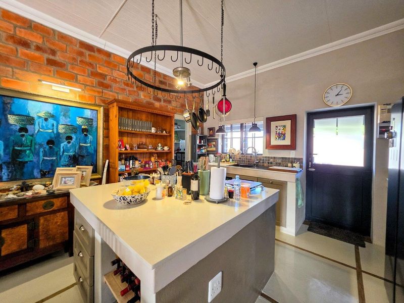 A characterful kitchen featuring an exposed brick wall, a central island with stone countertop, and a hanging pot rack, offering a warm, rustic aesthetic.