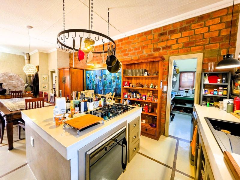 A rustic kitchen featuring an island with a gas cooktop, built-in oven, exposed brick wall, and a convenient adjoining scullery area.