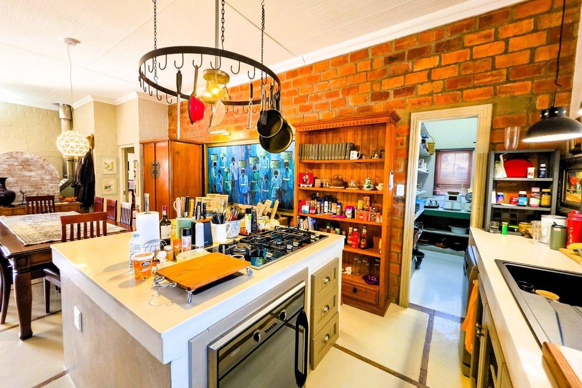 A rustic kitchen featuring an island with a gas cooktop, built-in oven, exposed brick wall, and a convenient adjoining scullery area.