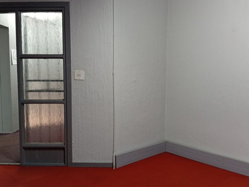 An empty hallway space featuring textured walls, red carpeting, and a glass-paneled door leading to an adjacent area.