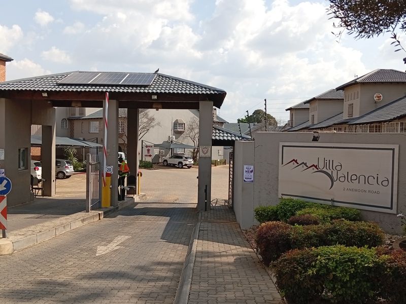 The secure entrance to Villa Valencia complex, featuring a gated access point, boom gate, and professional signage.