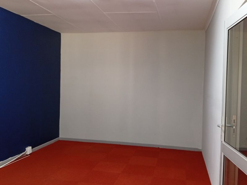 An empty office space featuring red carpet flooring, a blue accent wall, and a glass panel door.