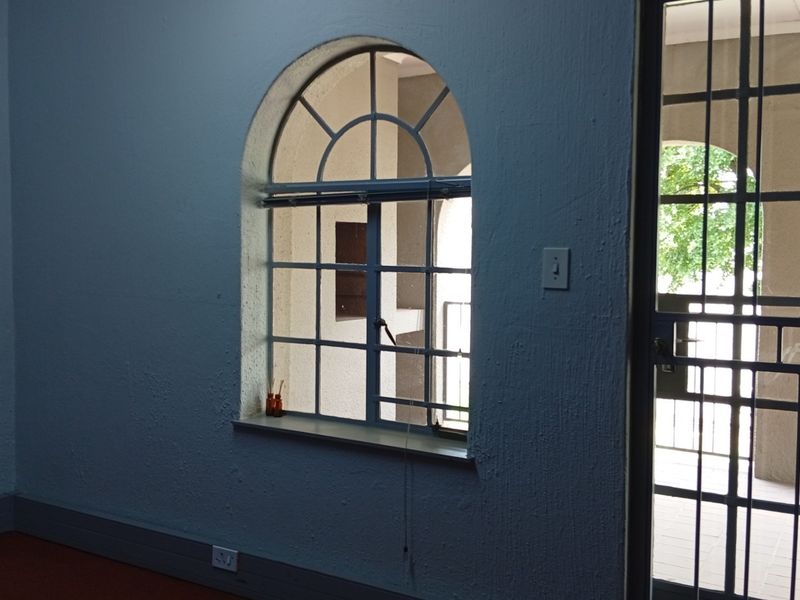 An empty office space featuring an arched window and a secure metal entrance gate, providing natural light and access to an outdoor area.