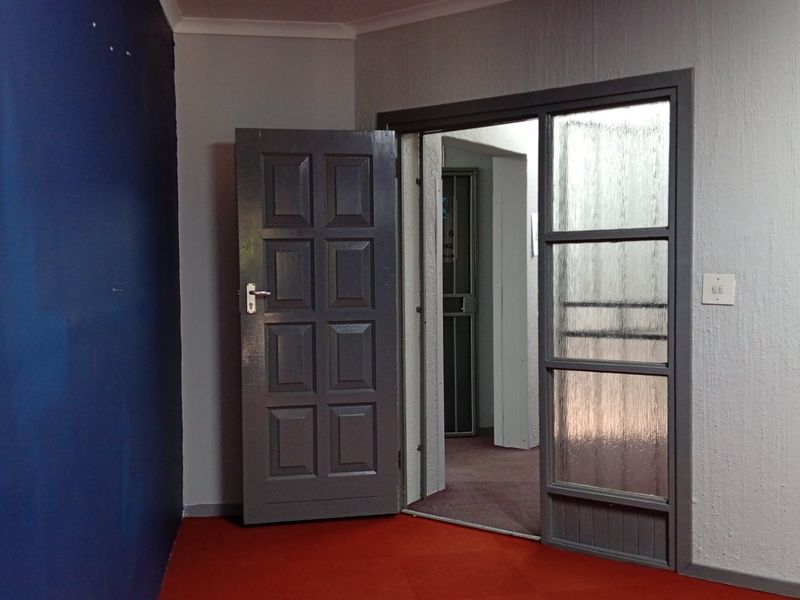An empty entry area featuring a panelled door and a glass-panelled door leading to an adjacent space with carpeted flooring.