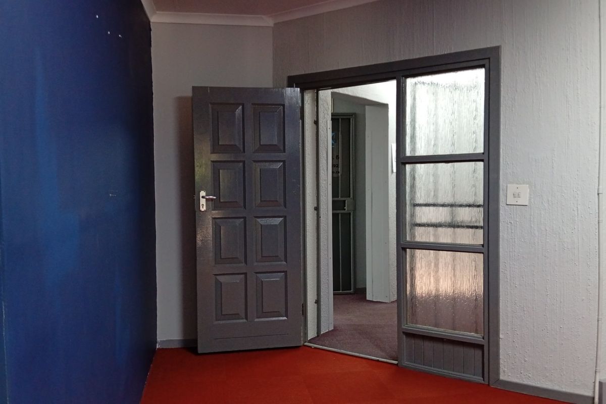 An empty entry area featuring a panelled door and a glass-panelled door leading to an adjacent space with carpeted flooring.