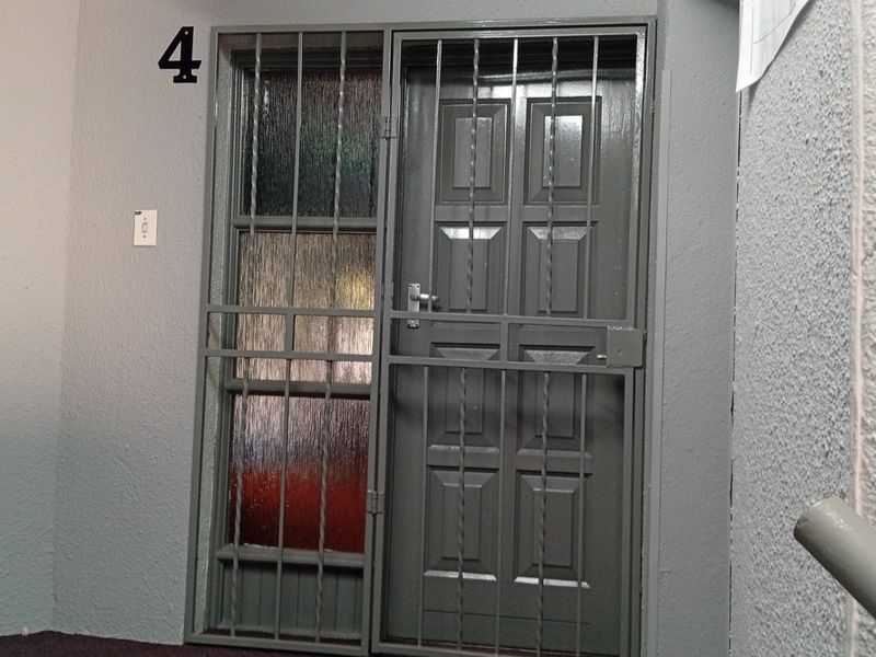 Entrance area featuring a secure metal gate and textured glass panel, providing a functional and secure access point to the unit.
