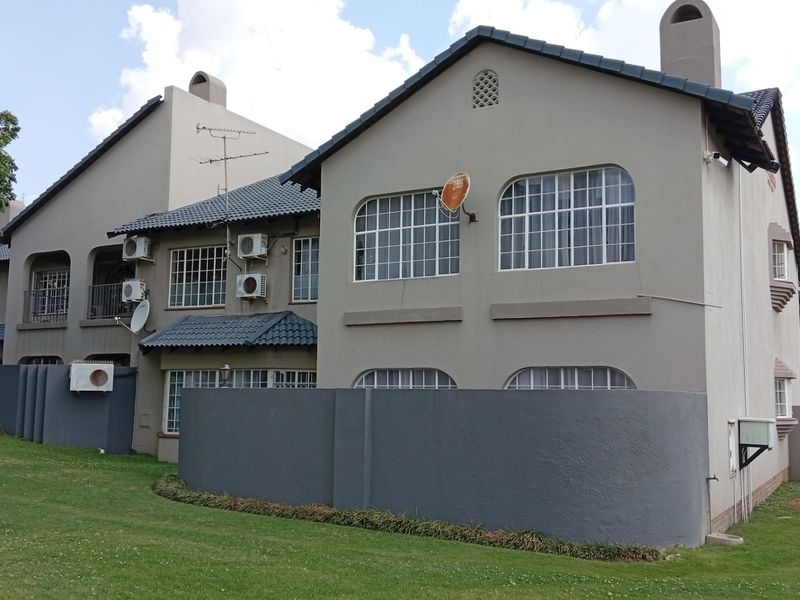Rear view of a multi-story residential complex featuring plastered facades, tiled roofing, arch-top windows, and established lawn areas.