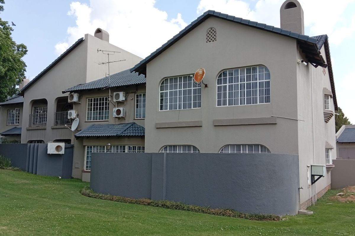 Rear view of a multi-story residential complex featuring plastered facades, tiled roofing, arch-top windows, and established lawn areas.