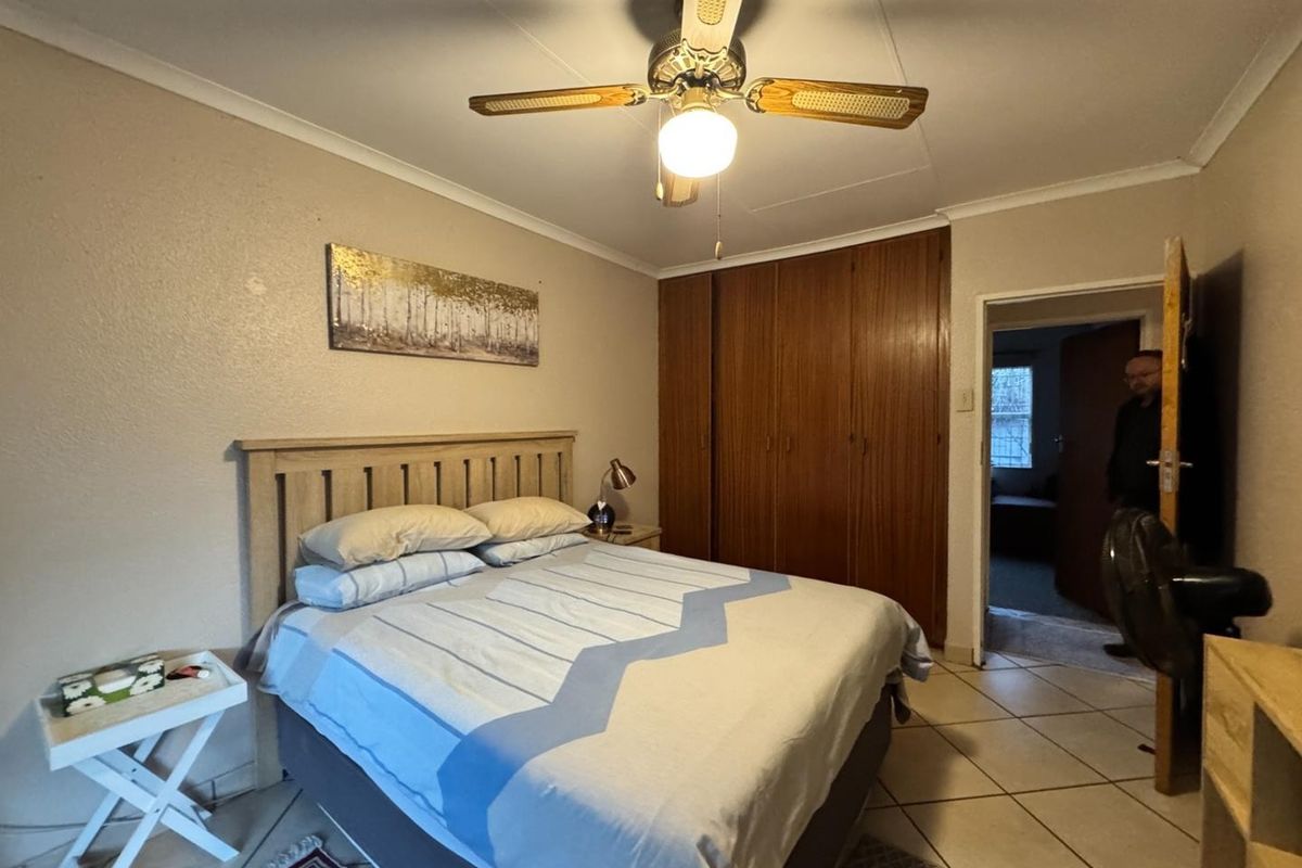 A functional bedroom featuring built-in wooden cupboards, a ceiling fan, and tiled flooring, offering a practical layout for comfortable living.