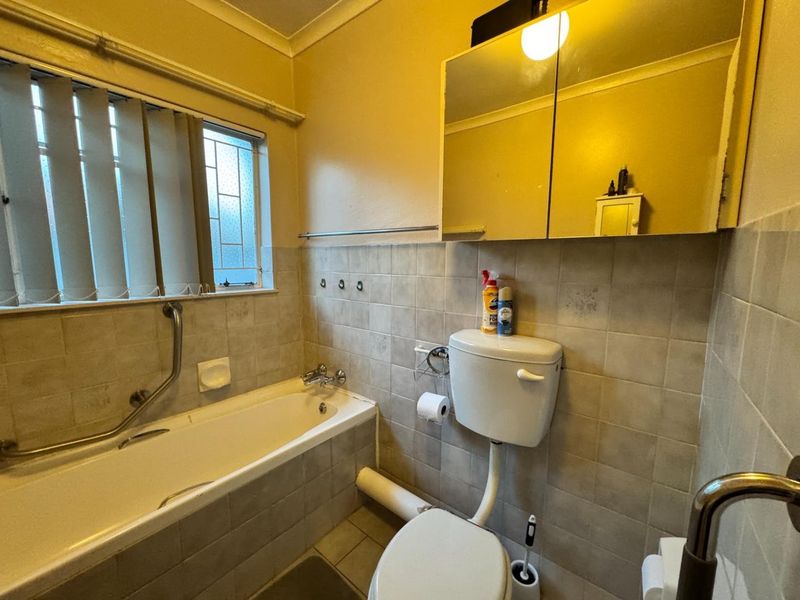 A functional bathroom featuring a bathtub, toilet, and mirrored medicine cabinet, finished with neutral wall tiles and equipped with safety grab rails.