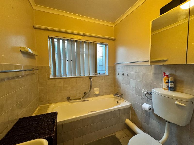 A functional bathroom featuring a bathtub, toilet, and tiled finishes. The space is dated and would benefit from modern updates to improve its aesthetic appeal.
