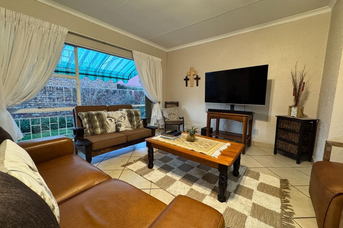 A comfortable living room featuring tiled flooring, a large window with an external awning, and neutral wall finishes.