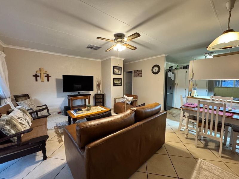 Open-plan living and dining area featuring tiled flooring, a ceiling fan, and integrated kitchen cabinetry, creating a functional and connected living space.