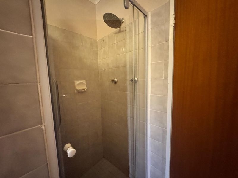 A functional shower enclosure featuring tiled walls, a fixed shower head, and a glass door, presenting a dated but well-maintained bathroom space.