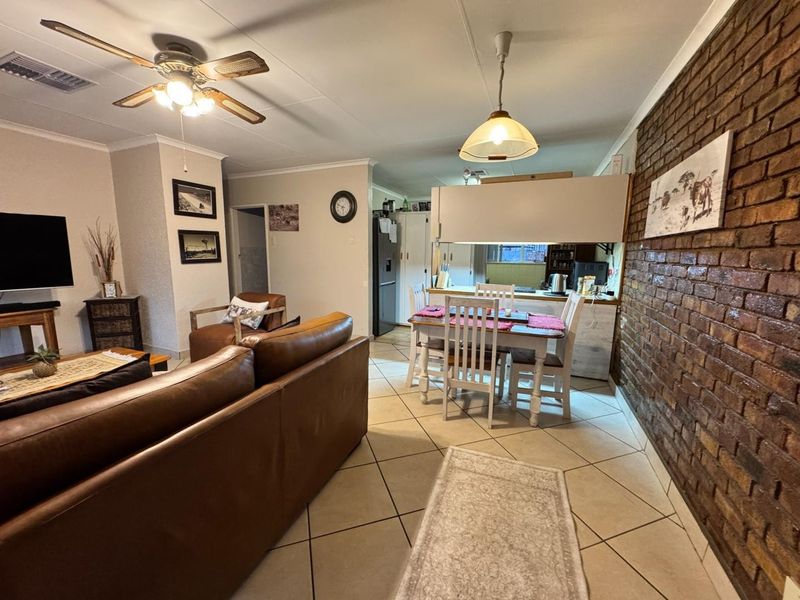 Open-plan living and dining area featuring tiled floors, a prominent exposed brick wall, and a ceiling fan, creating a functional and connected living space.