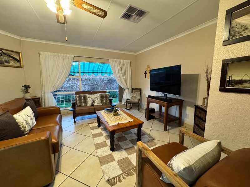 A comfortable living room featuring tiled flooring, a ceiling fan, and a large window that provides natural light.