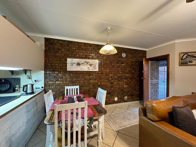 Open-plan living and dining area featuring an exposed brick wall, ceramic tile flooring, and integrated kitchen cabinetry with a functional layout.