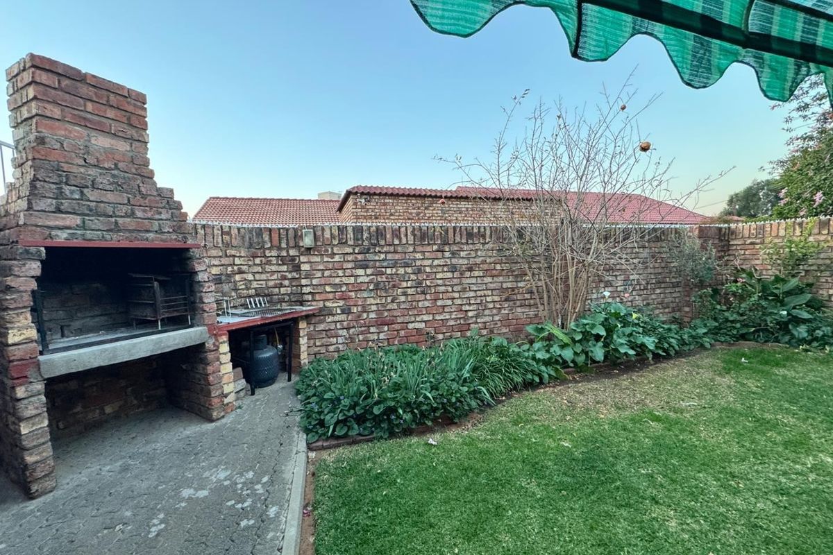 A private rear garden featuring a built-in brick braai, paved patio area, established garden beds, and a retractable awning for shade.